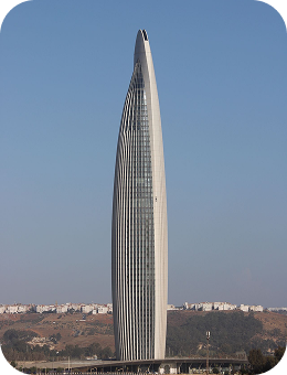 Tall modern skyscraper with curved design against a clear sky and distant city background.